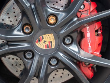 Cremona, İtalya 22 Ağustos 2025 Kırmızı Porsche fren kalibresi ve paslı cıvatalar, yüksek performanslı bir spor arabanın detaylarını gösteren siyah bir Porsche tekerleğinin arkasında görünür.