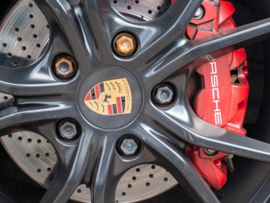 Cremona, İtalya 22 Ağustos 2025 Kırmızı Porsche fren kalibresi ve paslı cıvatalar, yüksek performanslı bir spor arabanın detaylarını gösteren siyah bir Porsche tekerleğinin arkasında görünür.