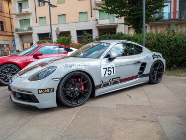 Cremona, İtalya 22 Ağustos 2025, özelleştirilmiş yarış Porsche 718 Cayman ile 751 numaralı kırmızı bir Porsche 911 'in yanındaki kaldırımlı meydanda park edilmiş, otomotiv tasarımı ve yarış ruhu sergilenmektedir.