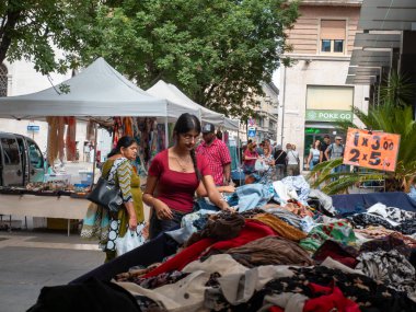 Cremona, İtalya 22 Ağustos 2025 'te güneşli bir yaz gününde, İtalya' nın Cremona kentindeki bir açık hava pazarında iki kadın kıyafetlerini karıştırırken diğer insanlar arka planda yürüyorlar.