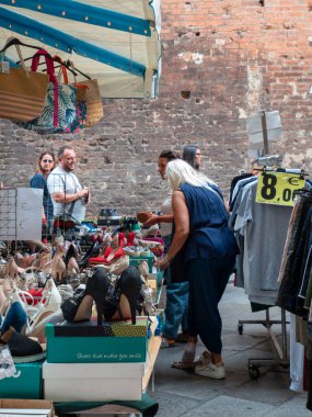 Cremona, Italy- 23 Ağustos 2025 Cremona Lombardy İtalya 'da güneşli bir günde açık hava pazarında renkli giysi ve ayakkabı tezgahlarına göz atan insanlar