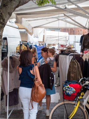 Cremona, Italy- 23 Ağustos 2025 İnsanlar yerel alışveriş odaklı güneşli bir gündüz sahnesinde Cremona Lombardy İtalya 'nın tarihi şehir merkezindeki açık hava pazarında kıyafetlerini tarıyorlar.