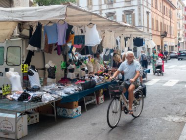 Cremona, Italy- 23 Ağustos 2025 Yaşlı bir adam, tarihi İtalyan kasabasındaki açık hava pazarının önünden geçiyor. Giysileri ve aksesuarları satılık.