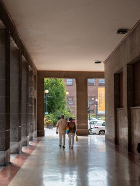 Cremona, Italya- 23 Ağustos 2025 Yaşlı çift, güneşli bir günde Avrupa 'nın bir şehrinde, mimari ve ağaçlarla çevrili bir sütundan el ele yürür.