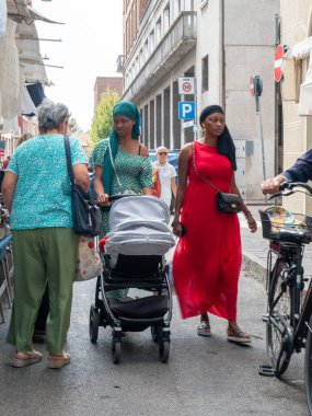 Cremona, Italy- 23 Ağustos 2025 'te, güneşli bir günde Cremona İtalya' da bir cadde boyunca yürüyen, bebek arabalı bir kadın ve yaşlı bir kadın da dahil olmak üzere çeşitli insanlar