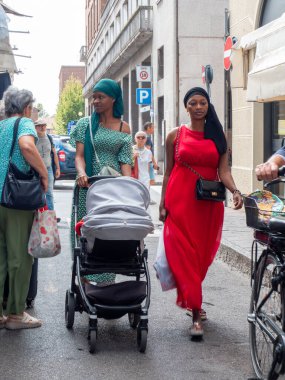 Cremona, Italya- 23 Ağustos 2025 Afrika kökenli iki genç kadın, Cremona Lombardy İtalya 'da güneşli bir öğleden sonra gezintisinin tadını çıkaran bir bebek arabasını ittiler.