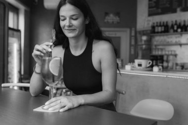 Genç bir kadın, güneşli bir öğleden sonra şık bir barda serinletici bir aperatif içecekten hoşlanır. Rahatlamış ve mutlu hisseder.