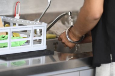 Cremona, İtalya - 21 Temmuz 2025 'te paslanmaz çelik bir lavabonun içinde ellerini yıkayan bir kişinin ön planda günlük ev işlerini gösteren bir bulaşık rafı ile yakın plan çekimi