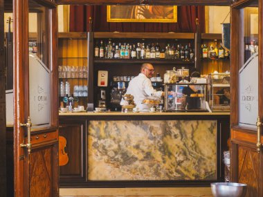 Cremona, İtalya - 3 Temmuz 2025 İtalyan bir barmen Cremona İtalya 'daki geleneksel bir kafede açık kapılar ardında görülebilen hamur işleri ve kahve makineleri ile mermer tezgahta çalışıyor