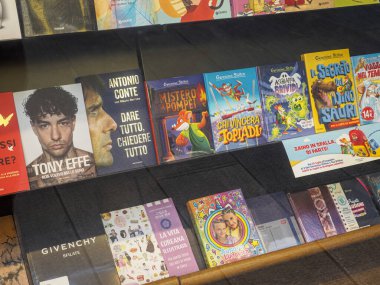 Milan, İtalya 14 Ağustos 2025 Romanlar, çocuk kitapları, biyografiler ve moda başlıkları içeren renkli edebiyat türleri Milano, İtalya 'daki kitapçı vitrininde güzelce sergilendi.