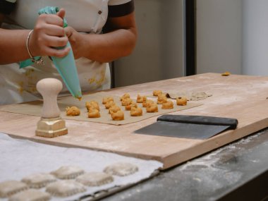 Genç bir kadının elleri, profesyonel bir mutfak ortamında pipo torbası kullanarak lezzetli İtalyan dolgulu tortelli makarna ustalıkla hazırlıyor.