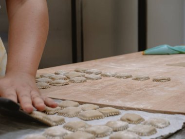 Profesyonel bir mutfak ortamında, un tozuyla süslenmiş geleneksel İtalyan dolgulu tortelli makarnasını ustalıkla hazırlayan genç kadın ellerini kapat. Ev yapımı lezzetli yemekler yap.