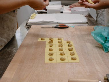 Profesyonel bir mutfak ortamında geleneksel İtalyan tortelli makarnasını titizlikle hazırlayan yetenekli eller bir mutfak başyapıtı için gerekli malzemeleri hazırlıyor.