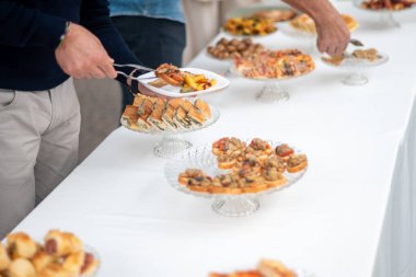 An elegant private event features guests selecting delicious appetizers and entrees from a beautifully arranged buffet table laden with various culinary delights