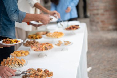 Guests enjoy a delicious spread of catered food at a sophisticated private event buffet with a variety of savory and sweet options on a white tablecloth adorned with ornate dishes and platters serving