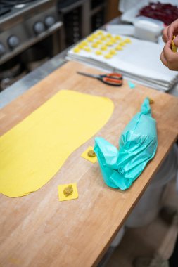 Fresh homemade pasta dough ready for ravioli filling with a chef's hands preparing more delicate pasta shapes in the background