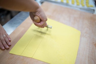 Close up of a person using a pasta cutter wheel to slice fresh yellow egg pasta dough on a wooden surface for homemade Italian cuisine