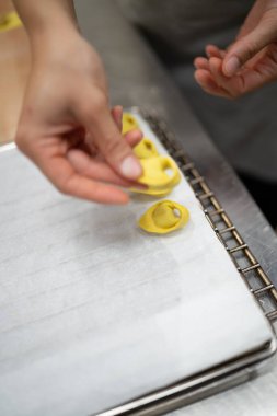 Close up of a pair of hands meticulously crafting delicate fresh pasta shapes on a parchment-lined baking sheet in a professional kitchen setting