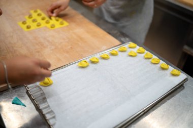 Hands carefully arranging small golden ravioli pasta shapes on a baking sheet lined with parchment paper in a professional kitchen setting