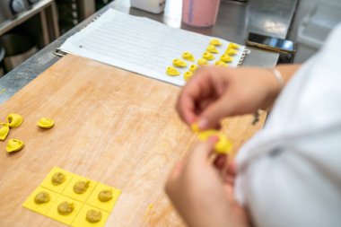 Close up on a person's hands carefully shaping fresh pasta dough into small stuffed dumplings ready for cooking and preparation in a bright kitchen setting
