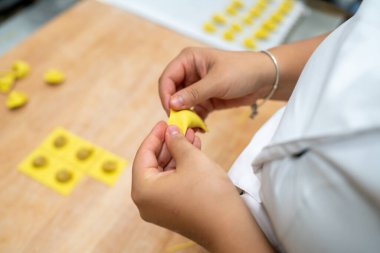 Close up of skilled hands carefully crafting delicate homemade tortellini pasta parcels with savory filling on a rustic wooden surface