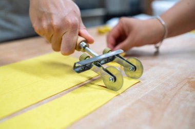 Homemade pasta making close up shot of hands using a pasta cutter to slice fresh dough into uniform strips for cooking