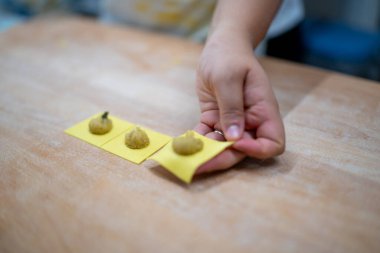 Homemade fresh pasta making process with skilled hands carefully filling small ravioli with savory filling on a wooden board a close up detail shot