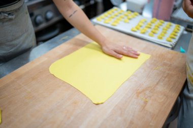 A culinary artist's hands gently press and shape fresh yellow pasta dough on a rustic wooden surface preparing for a delightful homemade meal