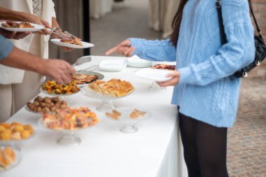 People enjoying a delicious buffet with an assortment of appetizers and pastries arranged beautifully on a white tablecloth elegant event