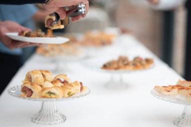 Close up of someone picking up a delicious pastry from a catered party spread of appetizers on a long white table