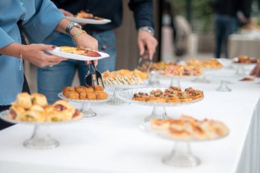 People gathering around a long table filled with an assortment of delicious appetizers and finger foods displayed on elegant tiered stands for a catering event