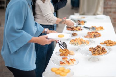 People enjoying a delicious buffet spread at an outdoor event with various appetizers and finger foods served on a long table creating a festive atmosphere for guests