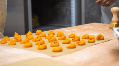 Passionate Chef Carefully Forms Vibrant Orange Gnocchi Dough Shapes on Rustic Wooden Surface in a Professional Kitchen Environment Capturing the Essence of Italian Culinary Craftsmanship