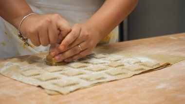 Hands carefully cutting fresh homemade pasta squares for authentic Italian cuisine preparation with intense focus in a warm kitchen environment