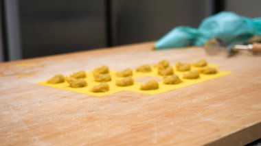 Close up of fresh vegetarian stuffed tortellini being carefully prepared by hand on a yellow pasta sheet with focus and passion in a professional small business kitchen during the fall season