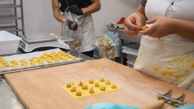 Artisan culinary artists meticulously handcrafting traditional Italian tortellini pasta with focus and passion in a small professional kitchen environment close up detail