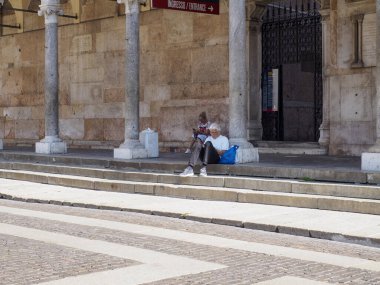 Cremona, Italy - September 18th Serene Elderly Woman Finds Momentary Respite on Ancient Stone Steps Beneath Classical Architecture in Northern Italy