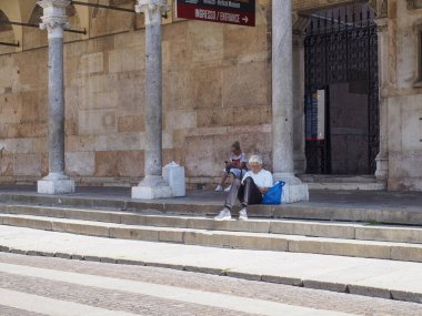 Cremona, Italy - September 18th Elderly Woman Sits on Ancient Stone Steps Outside a Historic Italian Building Enjoying a Quiet Moment Reading a Book on a Sunny Afternoon in Lombardy Italy
