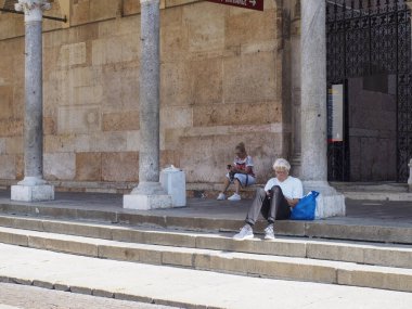 Cremona, Italy - September 18th People resting on stone steps outside an ancient building with large columns on a sunny day in an Italian town