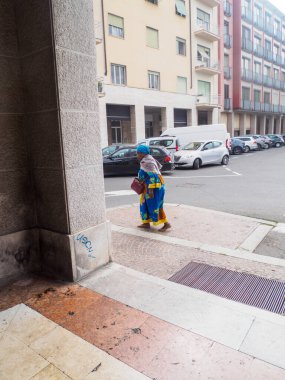 Cremona, Italy September 16th 2025 Elderly woman in traditional African attire and a colorful headscarf strolling along an urban sidewalk lined with parked cars and residential structures