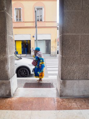 Cremona, Italy - September 18th 2025 Elegant woman in traditional colorful attire crosses a pedestrian street in a European city with modern architecture and shops creating a vibrant street scene