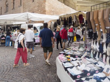 Cremona, Italy September 16th 2025 Visitors meander through stalls selling clothes and stockings beneath white awnings on a charming cobblestone road in a typical European marketplace