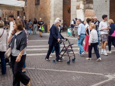 Cremona, Italy - September 18th 2025 Lombardy Italy town square vibrant street life with elderly woman using walker among diverse crowd enjoying a sunny day outdoors browsing market stalls near historic stone buildings
