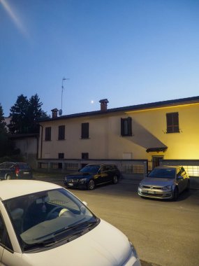 Cremona, İtalya - 28 Temmuz 2025 Alacakaranlıkta aydınlık bir binanın önüne park edilmiş açık mavi gökyüzü bir akşam manzarasını gösteriyor.