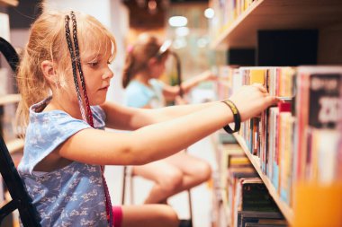 Okul kütüphanesinde kitap arayan liseli kızlar. Öğrenciler kitap seçiyor. İlköğretim. Ev ödevi. Kitaplardan öğreniyorum. Okula geri dön.
