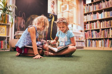 Two primary schoolgirls doing homework in school library. Students learning from books. Pupils having fun in library. Back to school clipart