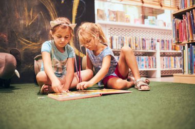 İki ilkokul öğrencisi okul kütüphanesinde bulmaca çözüyorlar. Öğrenciler kitaplardan öğreniyor. Öğrenciler kütüphanede eğleniyor. Okula geri dön.