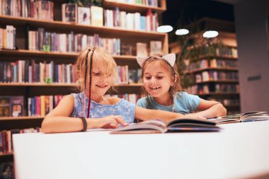 Okul kütüphanesinde ödev yapan iki ilkokul öğrencisi kız. Öğrenciler kitaplardan öğreniyor. Öğrenciler kütüphanede eğleniyor. Okula geri dön.