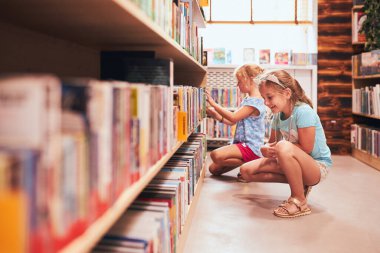 Two schoolgirls choosing books in school library. Primary school students learning from books. Children having fun in school club. Back to school. Doing homework clipart