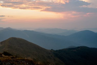 Dağlarda gün batımı. Aydınlatılmış sisli tepeleri, sisli yamaçları ve vadileri olan doğal dağ manzarası, turuncu sarı güneş ışığıyla mavi gökyüzü. Polonya 'daki Bieszczady Dağları' ndan inanılmaz bir manzara.